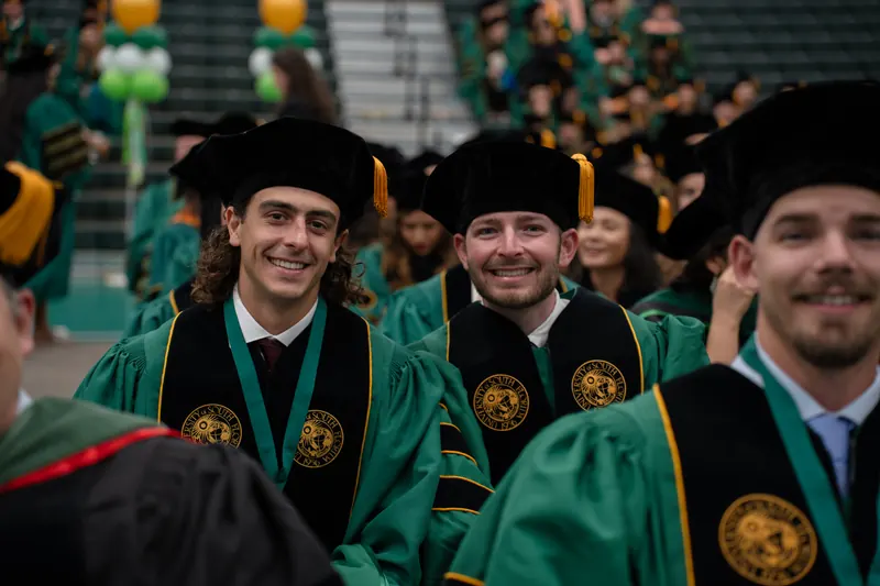 Doctoral graduates in green USF regalia smiling together at a commencement ceremony.